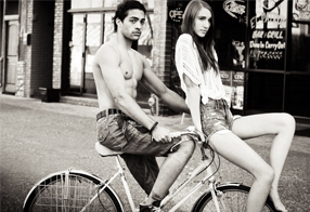 Young man with hair pulled into a bun and woman with long brown hair model while riding a bike in tandem into the distance toward photographer in the Quad CIties