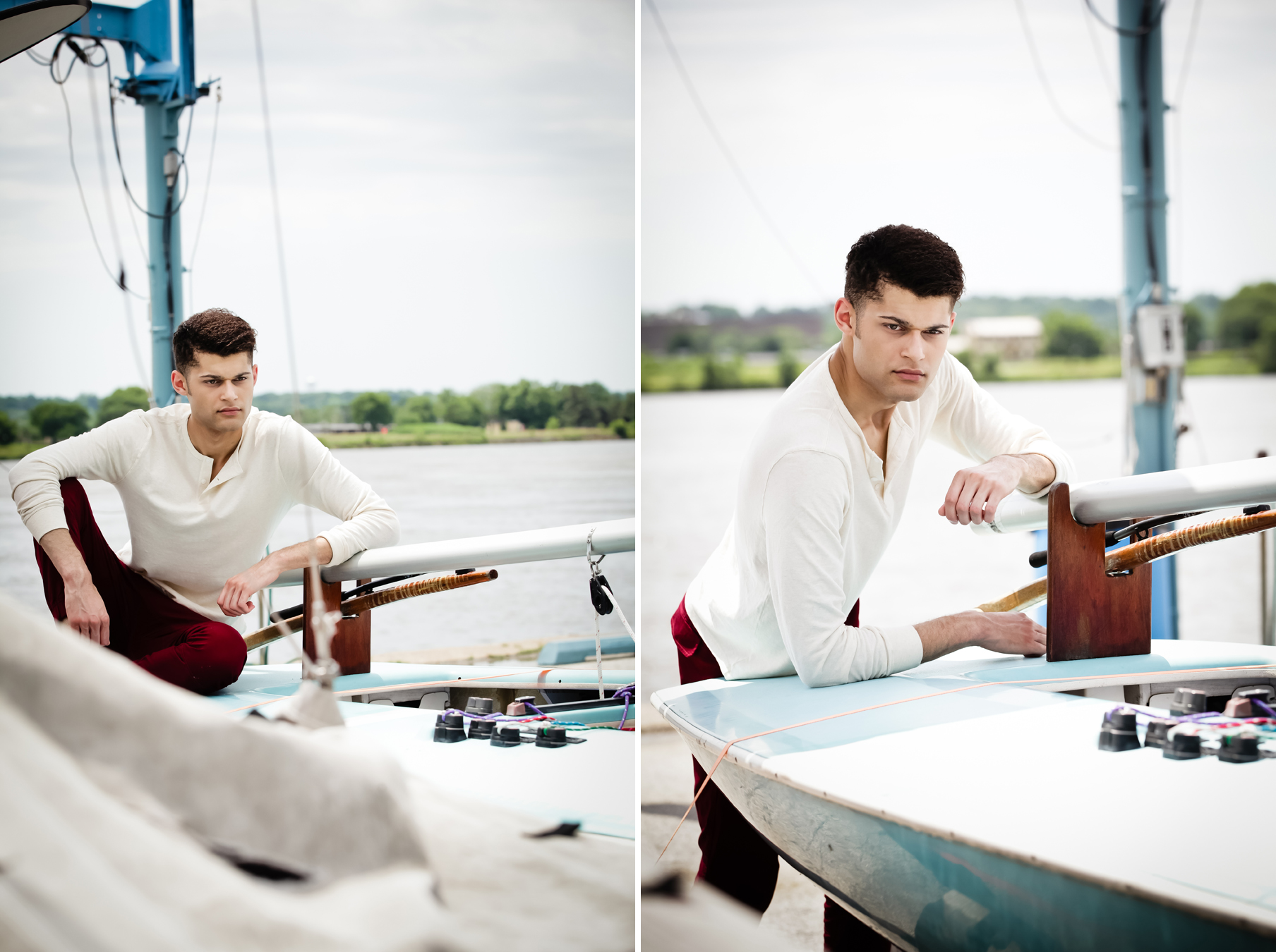 Young man with short curly hair models facing the photographer at a marina wearing a long-sleeved shirt and dark red pants