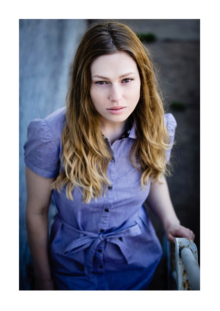 Female model with long, wavy brown hair faces the photographer wearing a blue button-up dress with puffed sleeves