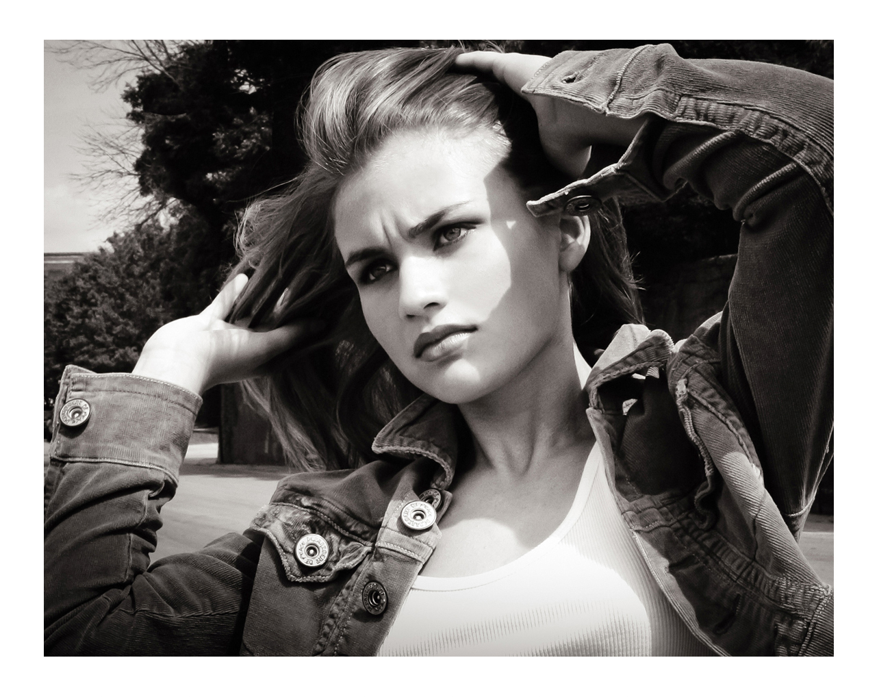 A young women with long brown hair models looking into the distance while wearing a thick jacket with many buttons and a white tank top