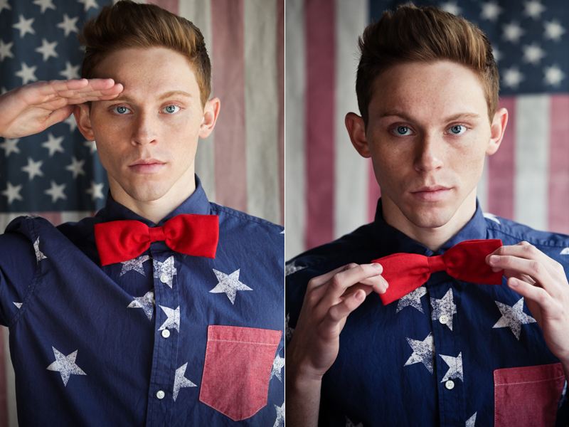 A young, auburn-haired male model in front of an American flag faces the photographer wearing a red, white, and blue outfit inspired by the American flag