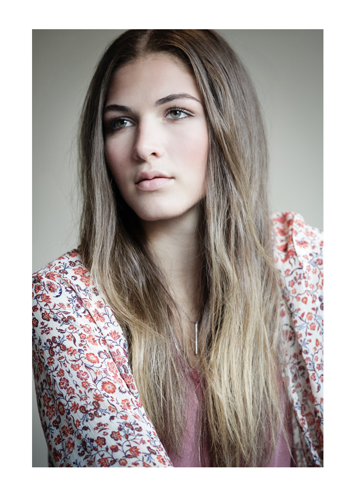 A young woman with long dark-brown hair models away from the camera wearing a red and white flower-print blouse