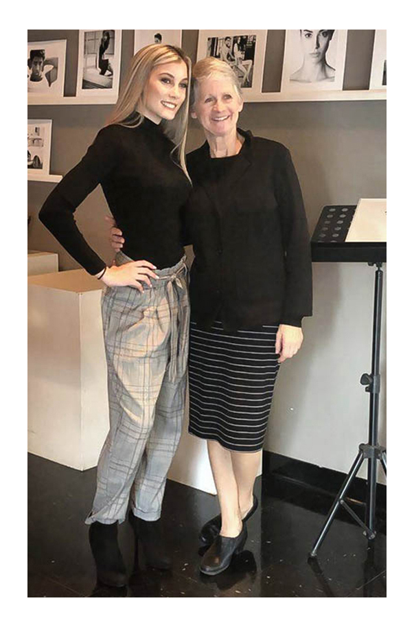 SK Models talent Anna smiles with owner Kay Schneider. Both are wearing black tops with a collection of talent photographs in the background